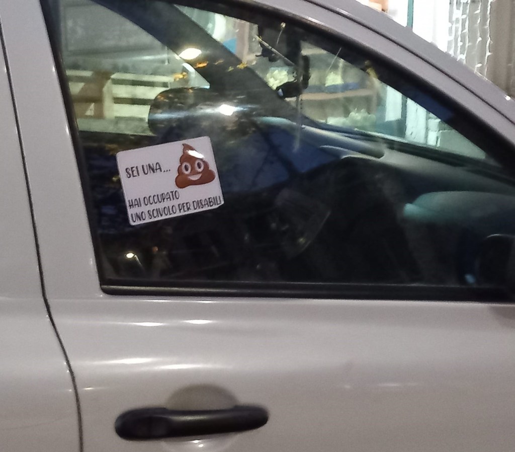 Adesivo stile "Brumotti" su una macchina parcheggiata davanti a scivolo per disabili